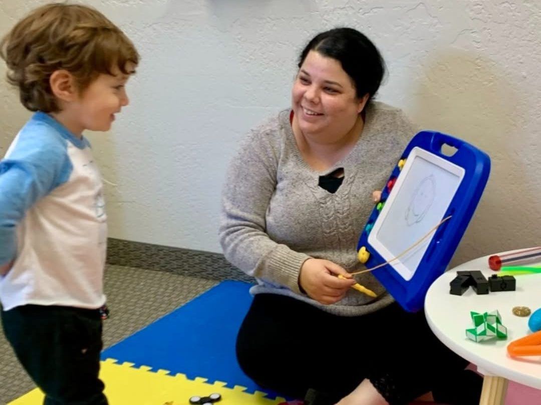 An Axis behavior technician and a young child smiling together during an ABA session