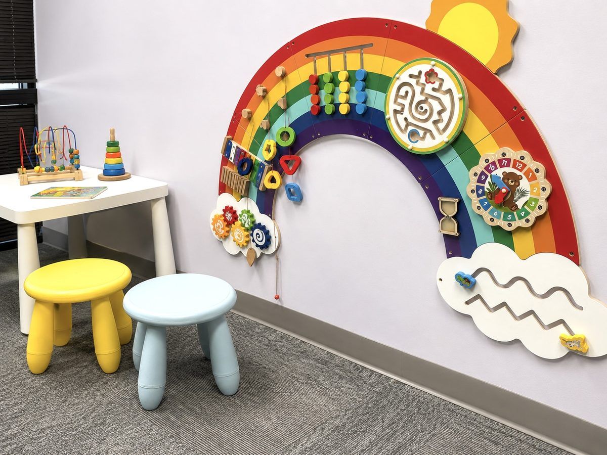 A rainbow sensory wall with activity panels beside a child-sized table in an Axis diagnostic clinic